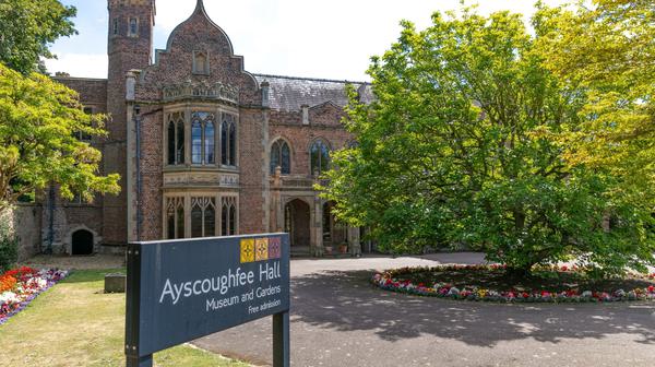 Exterior of Asycoughfee Hall with sign in front and trees under blue sky