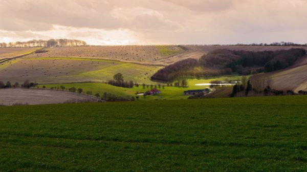 Big open farming fields in the distance with sun breaking through the clouds and casting glows on the rolling hills