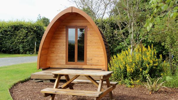 Camping pod nestled in greenery and trees with picnic bench out front