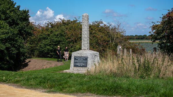 Mayflower pilgrim's memorial with two people walking in the background with blue skies and greenery all around