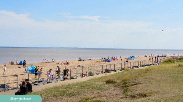 bustling seaside beach with grass in foreground and sea in background