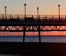 sunset over the coast line with wind turbines in the distance and pier in the foreground