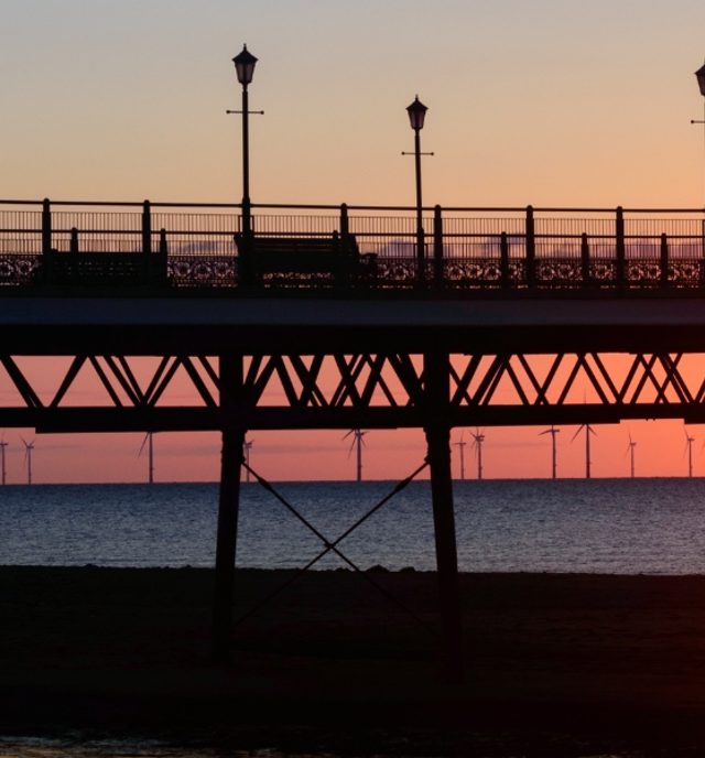 sunset over the coast line with wind turbines in the distance and pier in the foreground