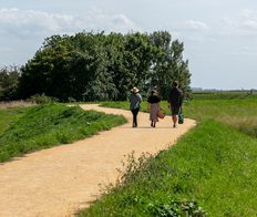 All weather path with 3 people walking along the middle, with a picnic basket in hand under clear blue skies surrounded by grass.